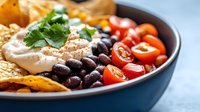 Colorful Mexican bowl with grilled chicken, black beans, cherry tomatoes, cilantro and tortilla chips for healthy lunch meal prep and restaurant menu.