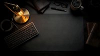 Overhead view of dark workspace with wireless keyboard, glowing vinyl record, coffee cup, notebook, and eyeglasses arranged on black surface for creative professional projects.