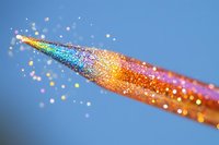 Magical rainbow glitter scattered from brush tip against blue background creates dreamy artistic composition with sparkling bokeh effect and vibrant colors.