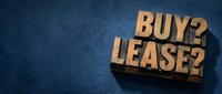 Wooden blocks spelling buy or lease on blue textured background, representing financial decision-making for business and real estate choices.