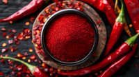 Ground red chili powder in black bowl with fresh hot peppers scattered around on dark wooden background, top view composition for food photography.