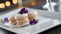French macarons with purple edible flowers on white ceramic plate, dusted with powdered sugar, elegant dessert presentation with soft bokeh background.