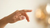 Woman hand reaching forward with elegant gesture against soft blurred warm background. Graceful feminine fingers extended in delicate motion for wellness concepts.