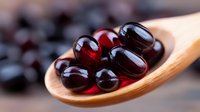 Red and black soft gel capsules on wooden spoon, close up view of dietary supplements and vitamins against blurred background. Medical and healthcare concept.