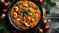 Traditional Spanish paella with seafood, rice and vegetables served in cast iron pan with Christmas decorations on rustic wooden background.