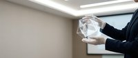 Professional businessman in dark suit holding transparent glass sphere in modern office environment with clean lighting and minimalist design.