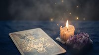 Mystical tarot card reading setup with burning candle and amethyst crystal on dark wooden surface creating magical atmosphere for spiritual guidance.