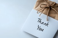 Gift box wrapped in gold paper with brown bow and thank you note on white background, elegant minimal composition for special occasions and gratitude.