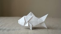 White origami fish crafted from folded paper, resting on a linen surface with soft neutral background, showcasing Japanese paper art.