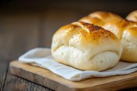 Fresh homemade dinner rolls with golden brown tops on rustic wooden cutting board with white linen napkin, soft and fluffy texture for food photography.