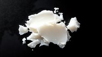 White coconut oil chunks and flakes scattered on dark surface for natural skincare and cooking applications.