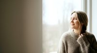 Thoughtful woman in casual sweater gazing out window with natural light, suitable for lifestyle, wellness, and contemplation themes.