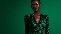 Young African woman in green leopard print dress poses confidently against emerald background, fashion portrait highlighting bold style and natural beauty.