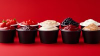 Assorted sweet and savory sauces in black portion cups on red background, featuring berry, chocolate and cream variations for desserts and appetizers.