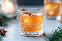 Festive winter cocktail with cinnamon stick and star anise garnish in crystal glass, pine branches and candle light creating cozy holiday atmosphere.