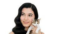Young woman with long black hair and East Asian ethnicity holding tabby and white kitten against white background, suitable for pet care, adoption, and lifestyle marketing.