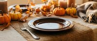 Autumn table setting with stacked plates, fork, knife, pumpkins, candles and neutral linens on burlap runner for fall dining and seasonal entertaining.
