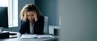 Stressed businesswoman holding head in hands at office desk experiencing work pressure and mental fatigue in corporate environment.
