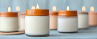 Minimalist arrangement of white scented candles in ceramic holders creating cozy atmosphere with soft glowing flames and warm orange lids on blue background.