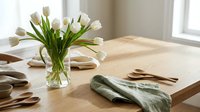 Fresh white tulips in glass vase on wooden table with green napkin and wooden utensils creating elegant dining room interior for spring home decor.