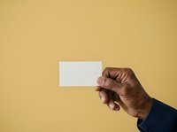 Hand of a dark-skinned male holding a blank white business card against a yellow background, suitable for branding, corporate identity, and marketing mockup designs.