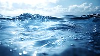 Clear blue ocean water surface with sunlight reflections and gentle waves creating dynamic ripples and movement. Underwater perspective shows depth and transparency.