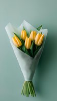 Fresh yellow tulips wrapped in white paper on mint green background. Minimalist spring bouquet with delicate flowers and green stems creates elegant composition.