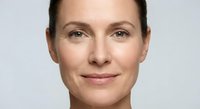 Close-up portrait of confident middle-aged Caucasian woman with natural makeup and pulled-back hair against neutral background for skincare campaigns.