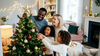 Diverse family decorating Christmas tree together in modern living room with festive lights and holiday ornaments during celebration.