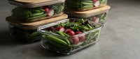Fresh mixed greens salad with radishes in glass meal prep containers with bamboo lids for healthy eating and food storage planning.