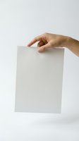 Hand holding blank white paper sheet against neutral background for mockup design templates and presentation materials.