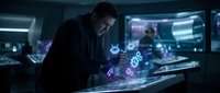 Man in dark business suit working with holographic digital interface displaying glowing purple and blue technology symbols in modern control room with multiple screens, representing cybersecurity and data analysis.