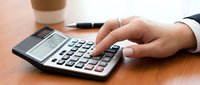 Professional businessman using calculator for financial calculations and budget planning at wooden desk in modern office environment.