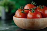 Fresh ripe tomatoes with water drops in wooden bamboo bowl on dark background with green herbs, macro food photography for healthy eating.