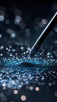 Makeup brush tip touching sparkling blue glitter powder against dark background, creating magical bokeh effect with scattered light reflections.