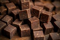 Dark chocolate cubes with rich texture and grainy surface scattered on wooden background, macro food photography for confectionery and dessert designs.