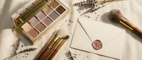 Luxury makeup palette with neutral eyeshadows, gold brushes, sealed envelope and dried lavender on silk fabric for beauty and cosmetics branding.