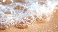 White soap foam bubbles on orange or copper colored surface with water droplets and soft focus macro photography creating abstract texture background.