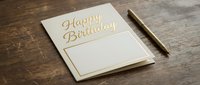 Elegant birthday greeting card with gold lettering and pen on rustic wooden table for celebration invitations and party planning.