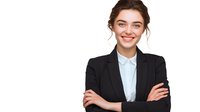 Young Caucasian businesswoman in black suit and light blue shirt smiling with arms crossed against white background, professional corporate portrait.