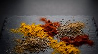 Colorful spice powder blend with cumin seeds scattered on dark slate surface for culinary cooking and seasoning applications in kitchen food preparation.