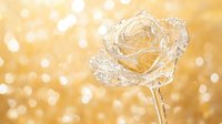 Delicate crystal rose sculpture against golden bokeh background creates magical atmosphere. Elegant glass flower art piece with sparkling reflections and dreamy light effects.