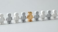 Wooden figure standing out among white paper cutout people in row, representing leadership, uniqueness and individuality in business teamwork concepts.