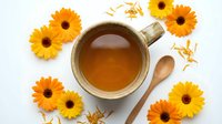 Herbal tea with fresh gerbera daisies and wooden spoon on white background, overhead view for wellness, natural remedy, and beverage design projects.