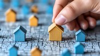 Hand placing wooden house model on city map for real estate investment planning and property location selection concept.