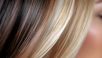 Close-up macro shot of blonde and brown hair highlights showing natural color transition and professional hair coloring technique for beauty salon advertising.