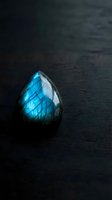 Polished labradorite gemstone with brilliant blue flash on dark wooden surface showcasing natural mineral beauty and iridescent properties for jewelry design.