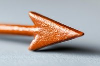 Metallic copper arrow tip in macro view against neutral gray background, showing detailed texture and directional pointing concept for business and navigation designs.