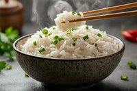 Steaming hot white rice garnished with chopped green onions in rustic ceramic bowl, with chopsticks lifting a portion for Asian cuisine presentation.
