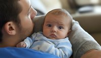 Tender moment between young father and baby in blue onesie. Close up portrait showing emotional bonding and paternal care during quiet family time at home.